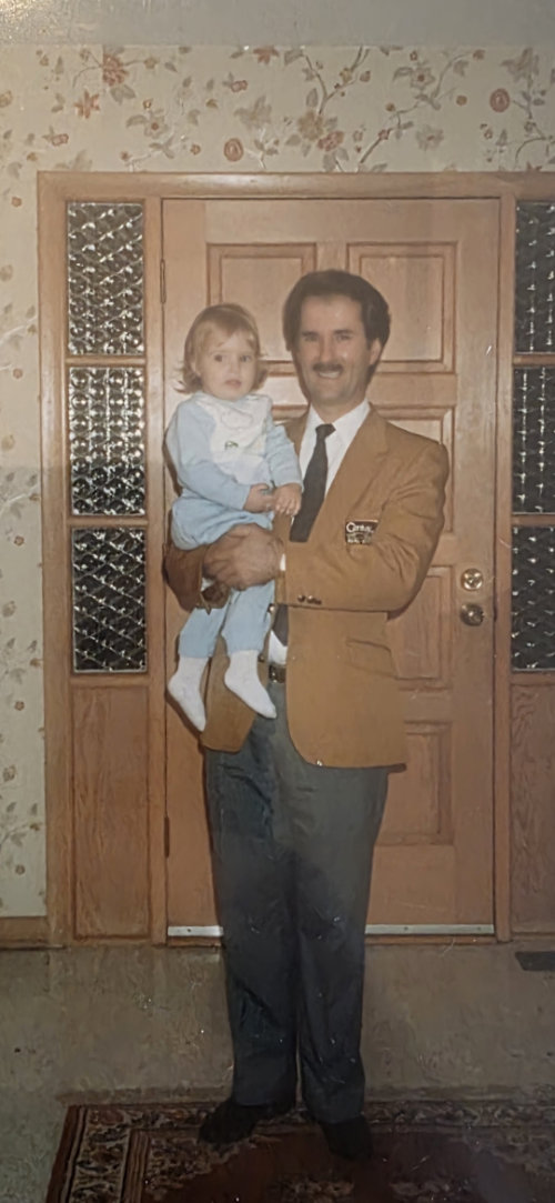 A father holding his young child in the entryway of a home
